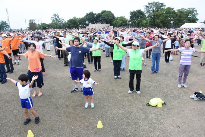 子供から大人まで、たくさんの参加者がラジオ体操を行なっている様子の写真