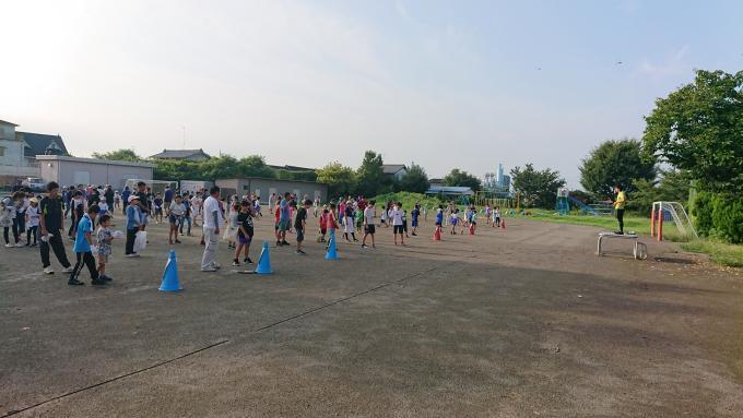 学校の校庭でたくさんの生徒が親と一緒にラジオ体操をしている様子の写真