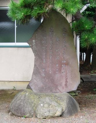 大きな岩の断面に文字が刻まれており、大きな岩の石台の上に置かれている万葉遺跡・防人藤原部等母麿遺跡の歌碑の写真