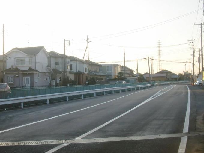 左側に住宅が立ち並び、住宅沿いの脇にガードレールが設置された道路の写真