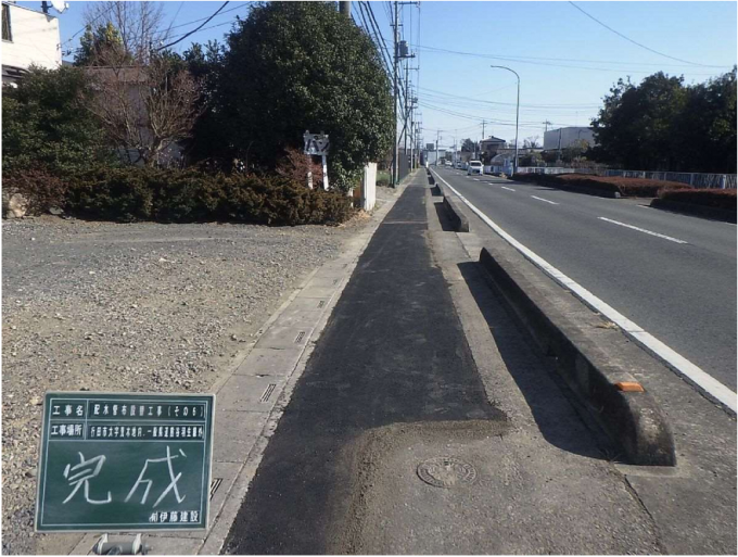 工事名、工事場所、「完成」の文字が書かれた工事現場用の黒板と工事が完了してきれいに舗装された歩道の写真