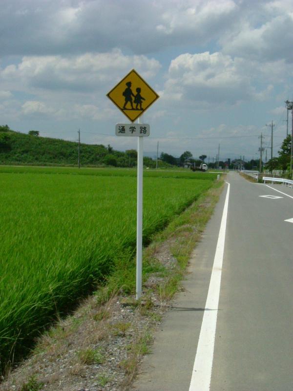 田んぼの横の道路脇に設置された警戒標識の写真