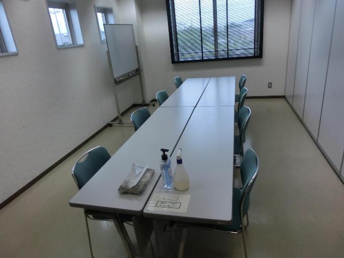 左方に移動式のホワイトボード、向い合せにテーブルと椅子が並べられた、研修室の写真