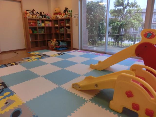 床にマットが敷かれ、滑り台、ぬいぐるみ、おもちゃのあるプレイルームの写真
