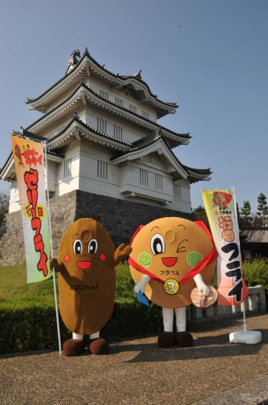 忍城の前で、ゼリーフライのぼり旗を持った「こぜにちゃん」と行田フライのぼり旗を持った「フラべぇ」の写真