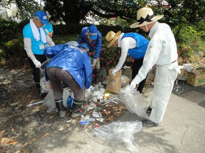 拾ったごみを地面に広げて分別し、袋に仕分けている清掃活動参加者の写真
