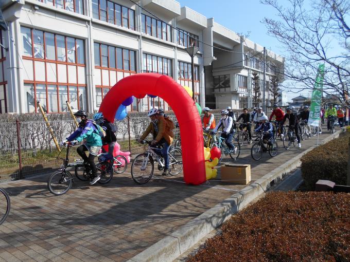 建物横の赤いエアーアーチに向かって自転車をこいでいるポタリングの参加者の写真