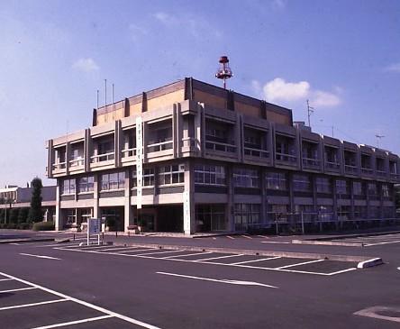 3階建ての行田市役所本庁舎の建物と広々とした駐車場の写真