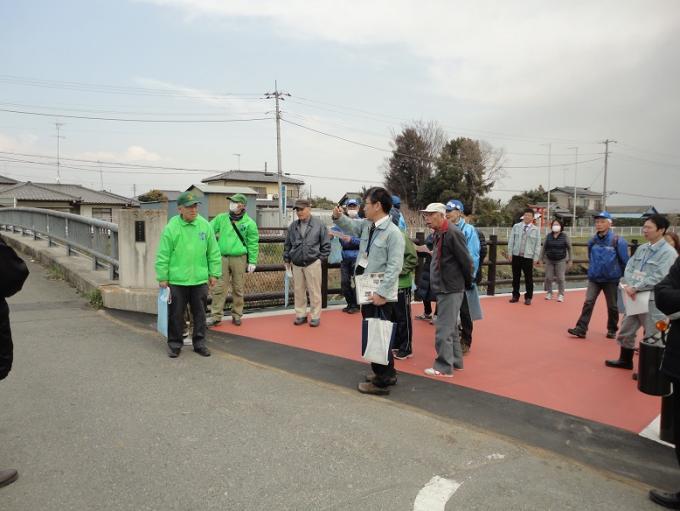 行田県土整備事務所の職員の男性の説明を聞きながら親水広場付近の歩道を歩く参加者の写真