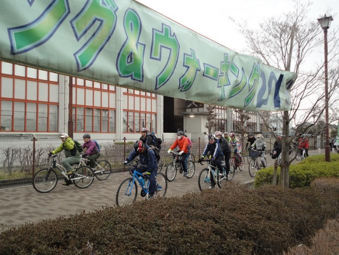 行田ふれあいポタリング＆ウォーキング2019の横断幕のかけられたコースを自転車に乗って走っていく参加者の写真