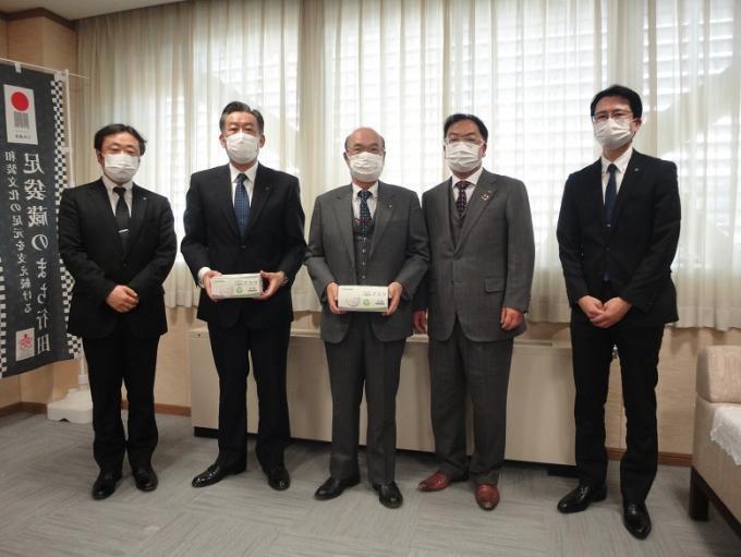 中央に石井市長、その両側に2名ずつ埼玉県北部地区郵便局長会の男性が立っており、石井市長と左から2番目の男性がマスクの箱を持っている写真