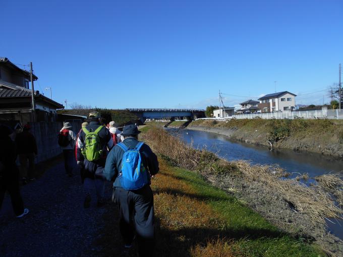 リュックを背負い帽子を被った参加者が忍川沿いの道を歩いている写真