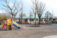 カラフルなコンビネーション遊具、木を囲むよう設置されている円形のベンチなどがある広々とした屋外公園の写真