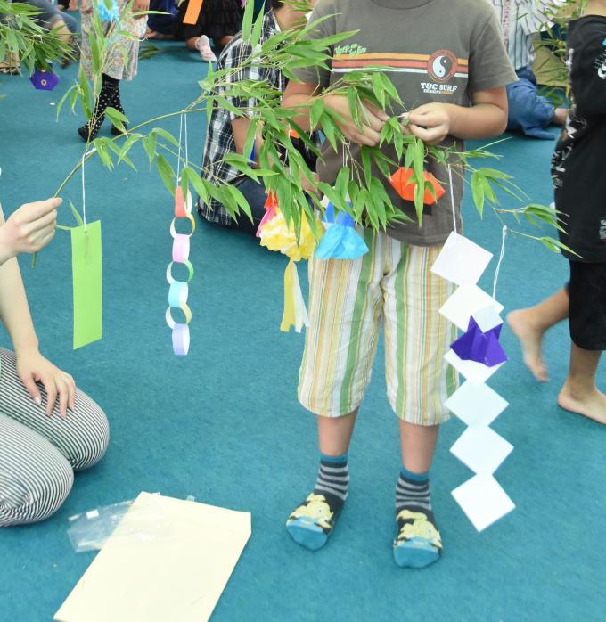 笹の葉に短冊や折り紙で作った飾りを括りつけている子供の写真