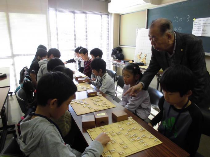 1対1で向かい合って将棋を指している子ども達と将棋盤を指さしながら指導をしている森先生の写真