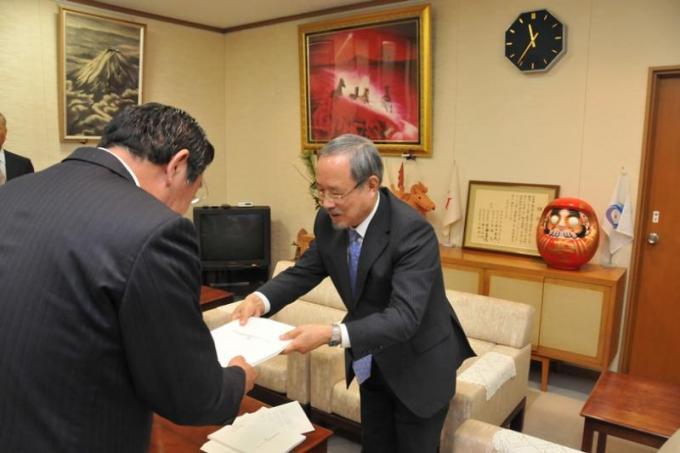 応接室で酒井委員長と吉田副委員長が工藤市長へ計画案を手渡している写真