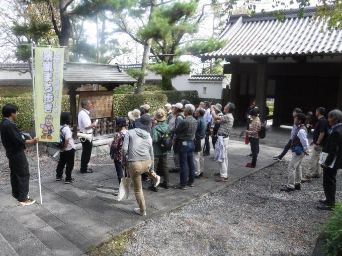 「景観まち歩き」の参加者が八幡神社の中にある看板の前で拡声器を持った年配の人から話しを聞いている様子の写真