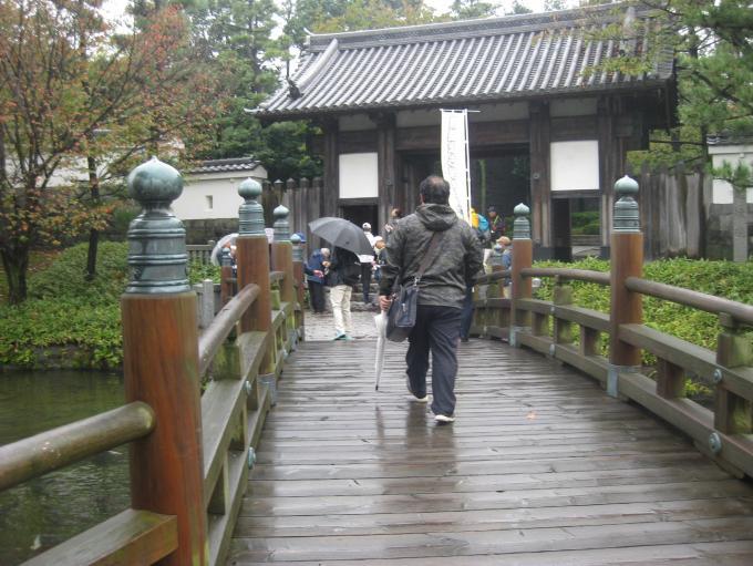 雨降る中、傘をさし忍城までのお堀に架かる木造の橋を渡る「景観まち歩き」の参加者の写真