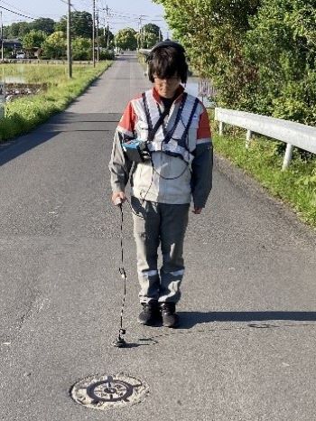 道路上で調査員が音聴機器を付けて音をきいている写真