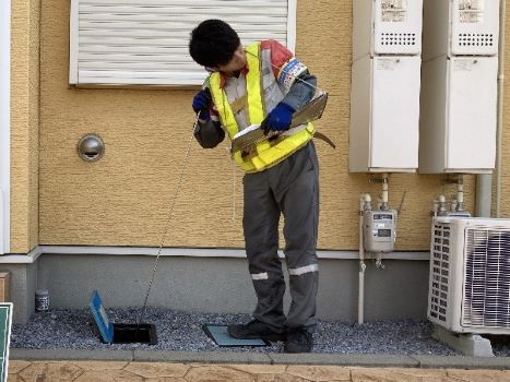 宅内の水道メーター付近で調査員が音聴機器を付けて音をきいている写真