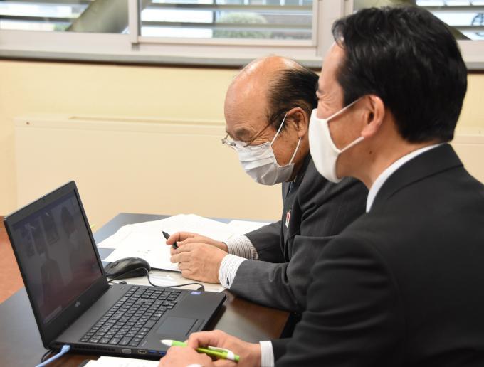 ペンを持ってパソコン画面を見ている石井市長と梁瀬議長を梁瀬議長の背後から撮影した写真