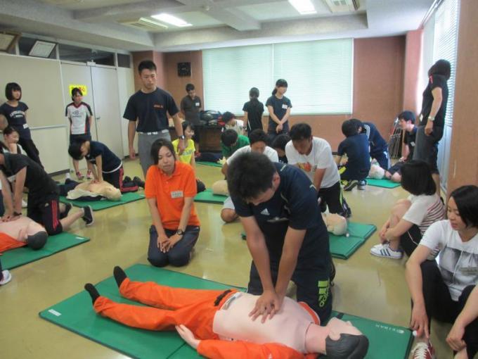 訓練用のマネキンに心臓マッサージをしている参加者と傍で見学している参加者の写真