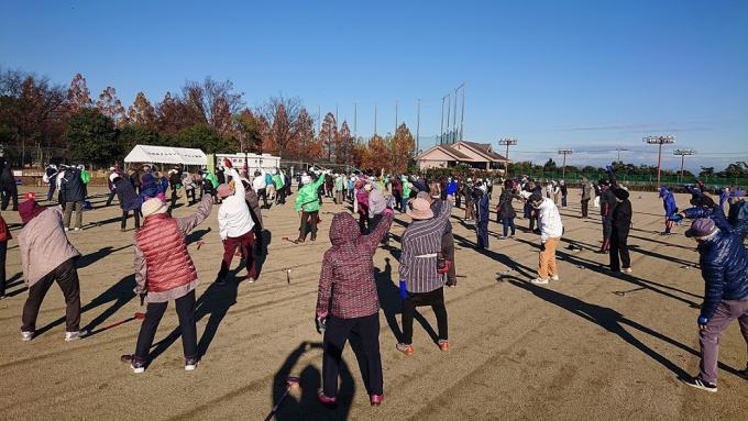 グラウンドに大勢の参加者が広がってラジオ体操を行なっている様子の写真