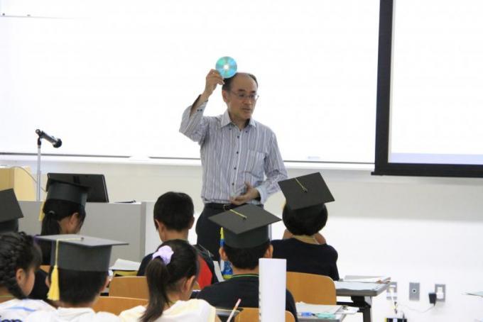 佐久田茂先生が光ディスクを見せながら子どもたちに話している様子の写真