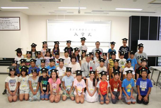 角帽子を被った子どもたちと大学稲永学長、森教育長との記念写真