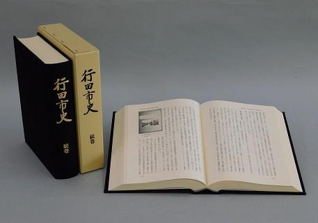 見開きになっている行田市史続巻の左側に黒い表紙の「行田市史 続巻」の本と本のケースが立てて並べてある写真