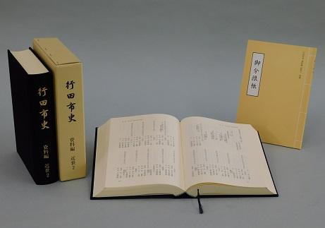 見開きになっている行田市史 資料編 近世2の左側に「行田市史 資料編 近世2」の本と本のケースが立てて並べて置いてあり、右側に薄い黄色の「御分限帳」が表紙を見せて立てて置いてある写真