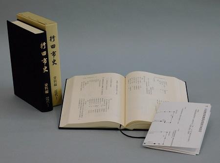 見開きになっている行田市史 資料編 近代1の右側に忍城城郭建物絵図が置いてあり、左側に「行田市史 資料編 近代1」の本と本のケースが立てて並べて置いてある写真