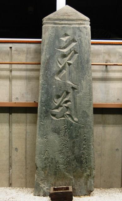 上部が三角に尖っており、その下に2段の線が刻まれ、正面に薬研（やげん）彫りで漢字が刻まれ、下段にも草書体で文字が記されている「大日種子板石塔婆」の正面の写真