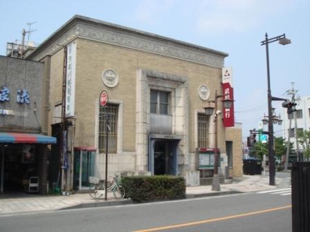 ベージュ色のスクラッチタイル貼りで、格子の入った縦長の窓が左右に見える近代復興式の鉄筋コンクリート造2階建ての武蔵野銀行行田支店店舗の外観写真