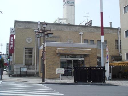 格子の入った縦長の窓や右側2階には小さい縦長の窓が並んでいる東側から見た武蔵野銀行行田支店店舗の外観写真