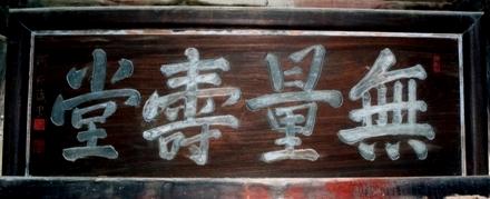 茶色の木材に白文字で無量壽堂と書かれた扁額の写真