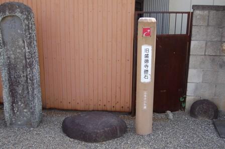 「旧盛徳寺礎石」と書かれた標識柱の左下にある平たい円形の礎石の写真