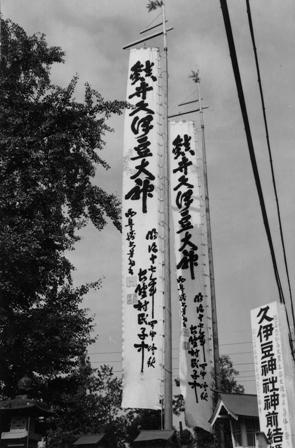 筆で文字が書かれた大きなのぼり旗2枚と久伊豆神社の看板の写真