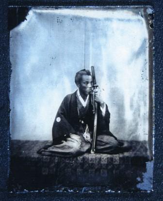 紋付袴を着て刀を左手に持って座っている武士が写っている写真