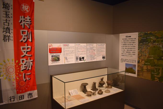 ガラスの展示ケースに飾られた埼玉古墳群に関する資料や解説などのミニパネルが展示されている写真