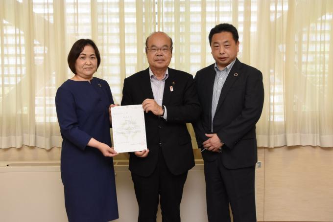 書面を一緒に持っている宇田祥枝社長と石井市長、その右側に立っている宇田栄治会長の写真